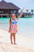 Little girl with toy airplane in hands on white sandy beach photo