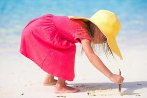 Adorable little girl drawing on white sand at the beach photo