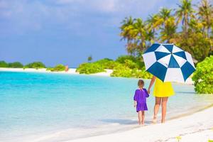 Mother and little girl with umbrella hiding from sun at beach photo