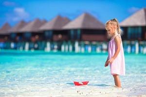 Adorable little girl playing with paper boat in turquoise sea