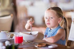 Adorable little girl having breakfast at outdoor cafe photo