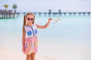 Little girl with toy airplane in hands on white sandy beach photo