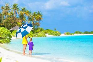 Mother and little girl with umbrella hiding from sun at beach photo