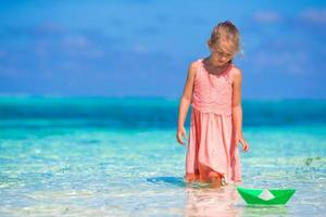 Adorable little girl playing with paper boat in turquoise sea