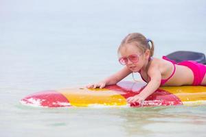 niña adorable en una tabla de surf en el mar turquesa foto