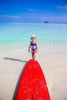 niña adorable con tabla de surf durante las vacaciones en la playa foto