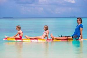 niñas pequeñas y papá joven en tabla de surf durante las vacaciones de verano foto