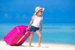 niña adorable con una maleta grande en una playa blanca tropical foto