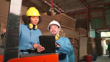Asian male engineer in safety uniform and hard hat and female worker colleague inspect storage, stock order at factory warehouse, piles of stacking cardboard manufacture, industry product management.