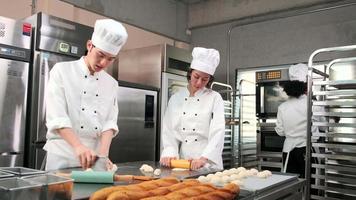 equipe gourmet profissional, três jovens chefs em uniformes e aventais de cozinheiro branco amassam massa de pastel e ovos, preparam pão e alimentos frescos de padaria, assando no forno na cozinha do restaurante de aço inoxidável. video