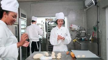 equipe gourmet profissional, três jovens chefs em uniformes e aventais de cozinheiro branco amassam massa de pastel e ovos, preparam pão e alimentos frescos de padaria, assando no forno na cozinha do restaurante de aço inoxidável. video