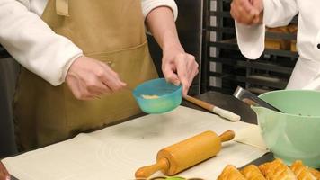 nelle riprese ravvicinate durante un corso di cucina, uno studente chef in uniforme con un grembiule sbatte le uova e mescola, si mescola con l'impasto di pasticceria e prepara ingredienti per prodotti da forno da forno, torta di frutta in cucina. video