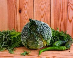 Savoy cabbage with pepper and greens on wooden background