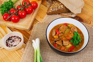 Stew with meat and vegetables in tomato sauce on wooden background photo