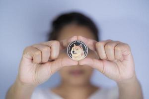 dogecoin doge incluido con criptomoneda a mano mujeres asiáticas que trabajan sosteniendo una moneda frente a la cara archivada y puesta y dármela. El futuro de la tecnología blockchain es el concepto dogecoin de cierre de dinero. foto