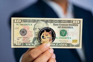 Dogecoin coin DOGE included with Cryptocurrency and stack 10 hundred new US dollar Money American on hand business man wearing a blue suit. Filed and put and give to me. photo