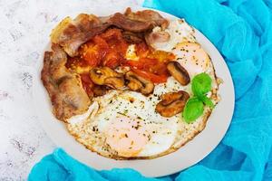 Fried eggs with bacon, tomatoes and mushrooms on white background. Top view photo