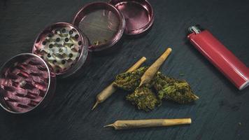 Marijuana buds and joint lie on a dark gray background. Grinder and lighter near cannabis photo