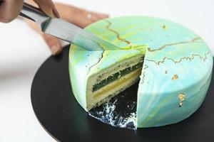 Close-up of cutting with knife mousse cake covered blue and green mirror glaze. French dessert. Frozen mirror icing on the cake. photo