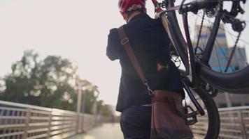 Back tracking view of an environmentalist in formal cloths carrying his bicycle to workplace, smart handsome cyclist traveling by sustainable transport and living a healthy lifestyle save planet, video