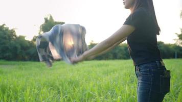 una trabajadora agrícola asiática de silueta se prepara para trabajar por la mañana en su campo de cultivo, una jardinera sacudiendo su camisa antes de usarla mientras disfruta de un pasto verde natural, mujer y belleza video