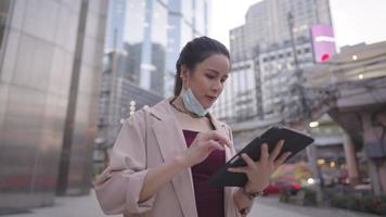 Asian attractive business woman checking on her mailbox and put on medical mask before leaving an office building, a dedicated employee scrolling on tablet while going home, e commerce activity video