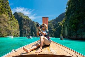 turista masculino tomando fotos en la proa de un bote de cola larga en una isla tropical, koh lipe, mar de andaman, tailandia.