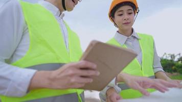 Closeup young active blonde woman holding an unfolded blueprint analyzing on building project with a surveillance of senior manager, environmental saving, using hand on tablet checks on briefing cases video