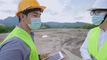 Two Asian outdoor worker man discussing work looking check and survey at the plain land site, inventing foreman giving advice and ideas, holding portable digital tablet using technology in the project video