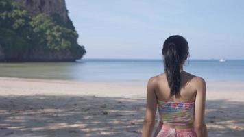 joven mujer asiática sexy camina hacia la costa de la isla bajo las sombras de los árboles, chica atractiva de vacaciones en una isla tropical, cámara lenta, vacaciones de verano en un resort de isla tropical, playa al aire libre día soleado video