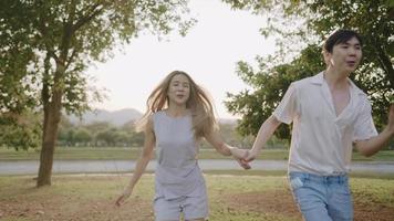 Two asian closed friend holding hands running cheerfully through summer meadow with the flare of day sunlight, people and relationship, young couple having a romantic time, stay by your side, video