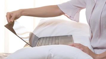 vista laterale ravvicinata della donna che lavora mani laptop aperti, lavoro confortevole a casa, posizionamento del computer laptop sul cuscino, inizio precoce del lavoro al mattino con luce solare calda attraverso la tenda bianca video