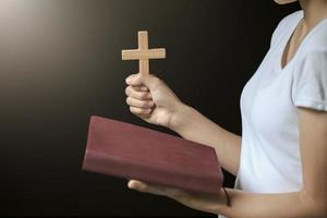Hands holding wooden cross over open russian holy bible on on sunrise background, Crucifix, Symbol of Faith. photo