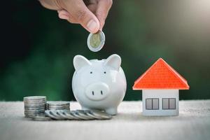 Female hand putting a coin into piggy bank, concept of saving money for house, Savings money for buy house and loan to business investment for real estate concept. Invesment and Risk Management.