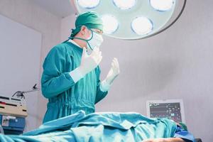 Male surgeon wearing surgical mask in operation theater at hospital, Patient on bed with medical team performing surgical operation in operating room photo