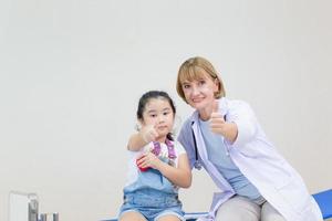 doctora y niña linda mostrando los pulgares hacia arriba. niño en consulta en el pediatra. conceptos de salud y medicina foto