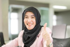 feliz mujer musulmana sonriente con hiyab mostrando el pulgar hacia arriba, alegre mujer de negocios musulmana dando el visto bueno en la oficina foto