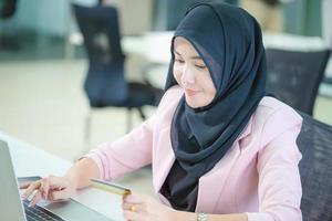 Portrait of a young Muslim businesswoman in an office, Young arabic woman in headscarf using laptop and credit card, shopping online concepts photo