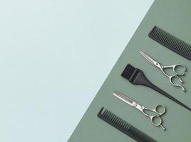 Hairdressing tools on a green background and a blue sheet with space for text. Black and steel hair salon accessories, comb and scissors. photo