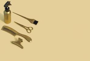 Gold hairdressing tools on a beige background. Template with hair salon accessories and space for text, top view. photo