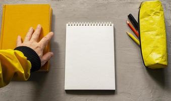 An empty white notebook, a book, and a yellow pencil case. Top view of objects. photo