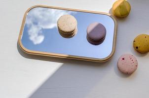 Macaroons of different colors on the mirror. A reflection of the sky and sweets on a white table. photo