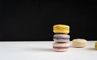 A stack of bright macaroons on a white black background. Dessert of yellow, purple and pink color close-up on the table. Banner, template with copy space photo
