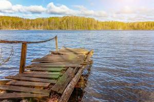 Fishing tourism relax concept. Traditional Russian Finnish and Scandinavian view. Beautiful forest lake or river on sunny summer day and old rustic wooden dock or pier. Fishing bridge on morning lake. photo