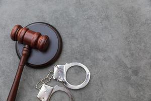 Law theme. Court of law trial in session. Judge gavel handcuffs on grey table in lawyer office or court session. Mallet of judge on concrete stone grey background. Justice human rights concept. photo