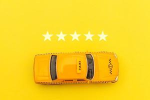 taxi de coche de juguete amarillo y calificación de 5 estrellas aislado sobre fondo amarillo. aplicación de teléfono inteligente del servicio de taxi para buscar en línea llamadas y reservar el concepto de taxi. símbolo de taxi. copie el espacio foto