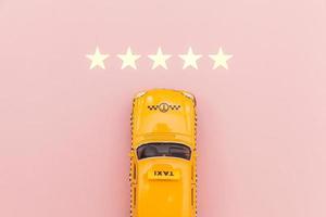 taxi de coche de juguete amarillo y calificación de 5 estrellas aislado sobre fondo rosa. aplicación de teléfono inteligente del servicio de taxi para buscar en línea llamadas y reservar el concepto de taxi. símbolo de taxi. copie el espacio foto