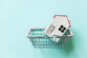 Simply design with miniature white toy house and supermarket grocery shopping basket isolated on blue background. Mortgage property insurance dream home concept Copy space photo