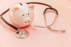 Medicine doctor equipment stethoscope and piggy bank isolated on pink pastel background. Health care financial checkup or saving for medical insurance costs concept. Copy space. photo