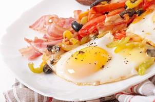 Breakfast - fried eggs with bacon, tomatoes, olives and slices of cheese photo